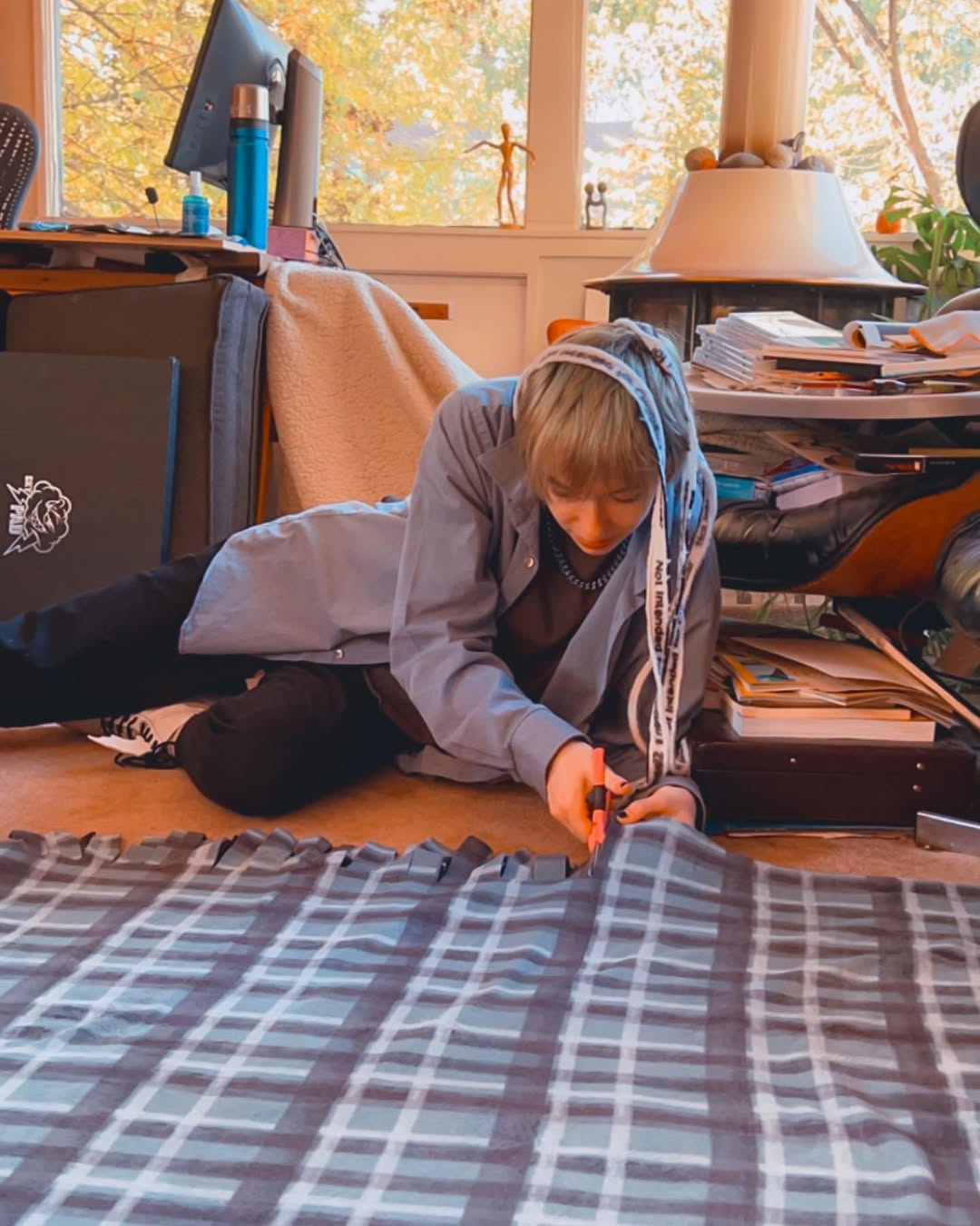 photo of cal laying down cutting strips for tie blanket with a strip of blanket draping over their head