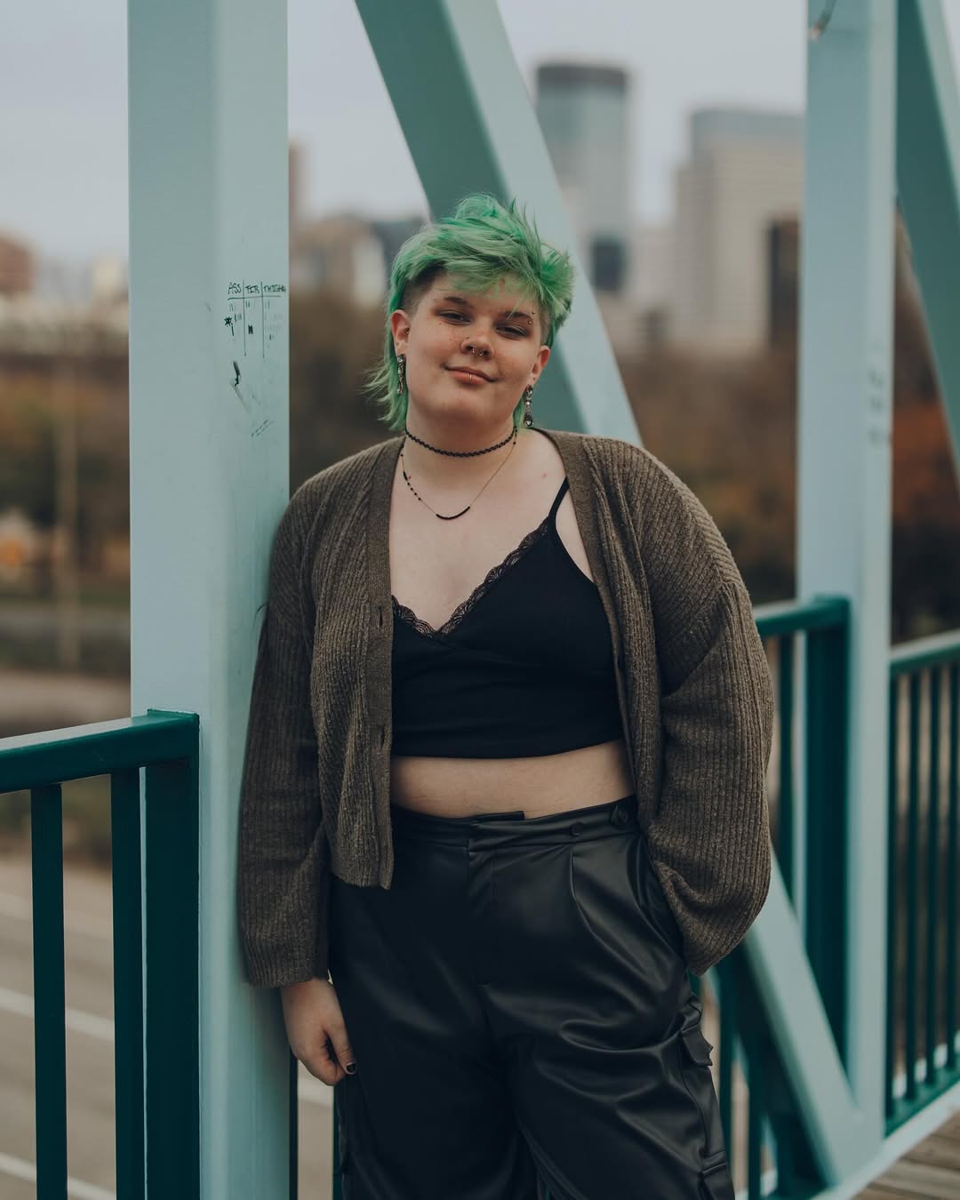 photo of amara in a cardigan, cropped lace top, and leather pants on a bridge